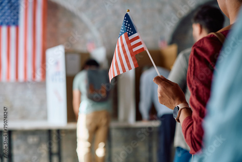 Close up of black woman holding US flag while waiting in line to vote during elections.