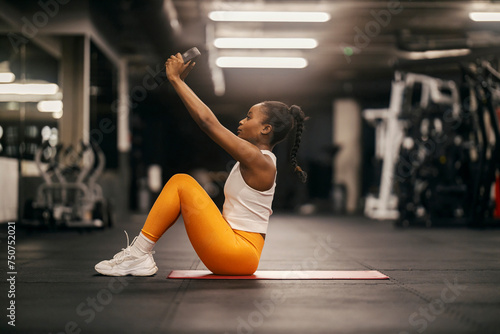 A strong black sportswoman practicing situps with weight plate at the gym.