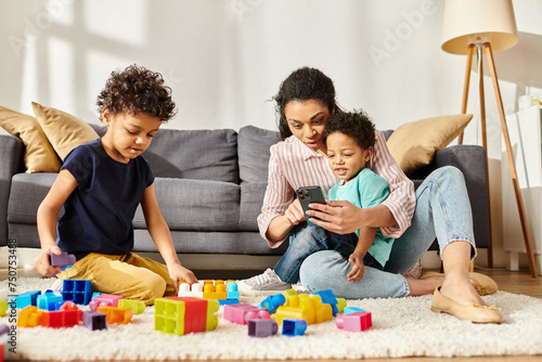 cheerful african american woman in homewear looking at phone while playing with her sons at home
