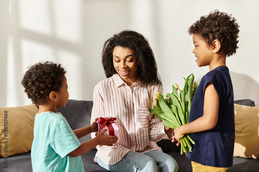 joyous african american woman receiving gift and tulips from her adorable sons on Mothers day