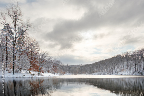 A wide angle view of a small lake in Indiana in the middle of winter on a snowy day with a mostly cloudy sky. The sun is bursting through the clouds and there are nice reflections on the water.  © Douglas