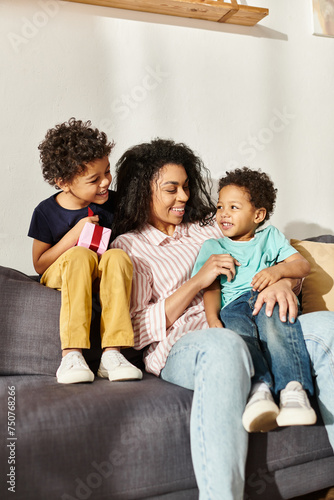 merry african american woman sitting on sofa with her cute children and having fun, Mother day