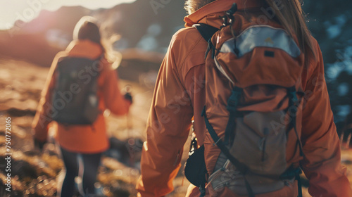 Two people are walking in the woods, one of them wearing an orange jacket and carrying a backpack