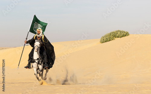 Saudi man in traditional clothing in the desert with a white horse, carrying a flag of Saudi Arabia