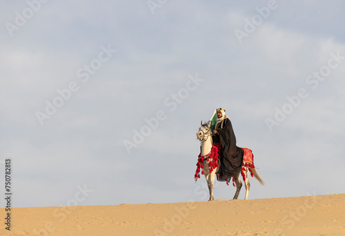 Man in traditional Saudi clothing in a desert with his  stallion