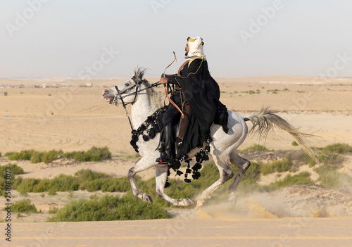 Saudi man in traditional clothing in the deset with a white horse photo
