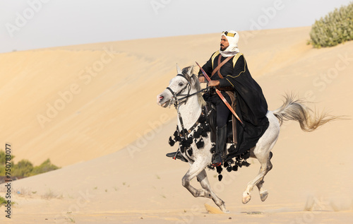 Saudi man in traditional clothing in the deset with a white horse photo