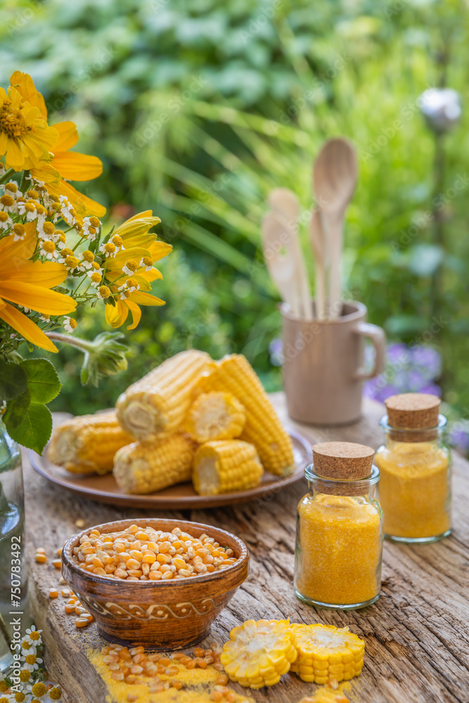 Kolby kukurydzy, ziarna i mąka kukurydziana na drewnianym stole w ogrodzie. - obrazy, fototapety, plakaty 