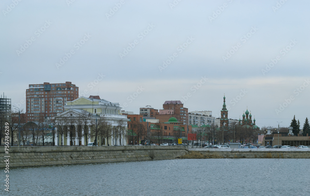 Naklejka premium A city landscape with a river and various buildings on a cloudy day