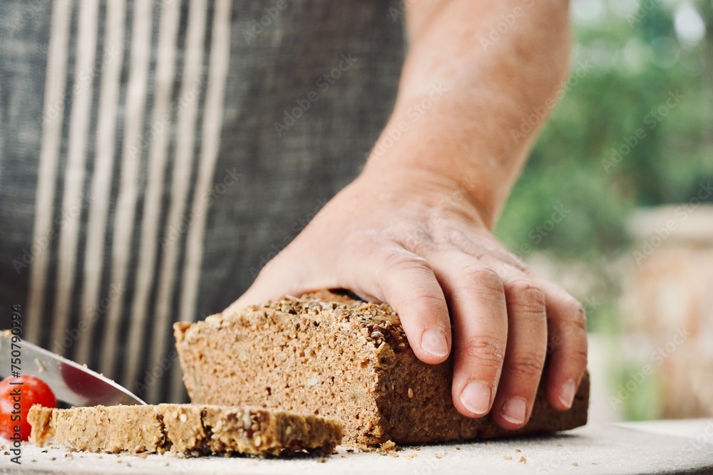 Woman in apron with close-up hands cutting homemade whole wheat bread. Woman in apron with close-up hands cutting homemade whole wheat bread.