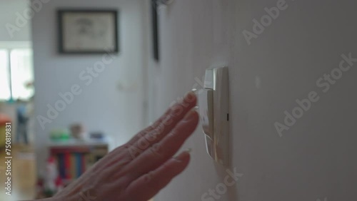 A close-up of a hand flipping a wall light switch in a cozy indoor setting, highlighting everyday routines and home functionality.