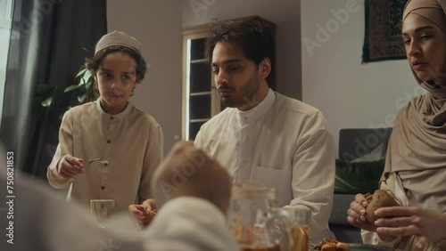Over shoulder footage of young muslim man eating pasty and speaking with family members during festive Eid dinner at home photo