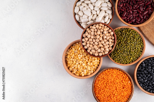 Various dried beans, lentils, mung, chickpea, pea assortment in wooden bowls. Legumes on white table top view. Vegan protein sources food, copy space