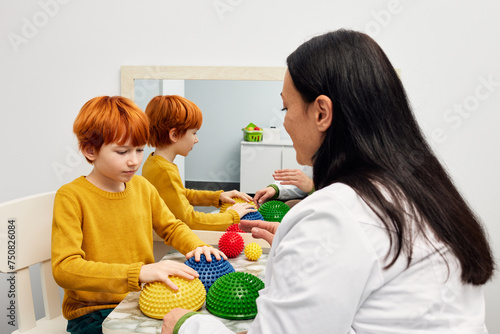 Occupational therapist using sensory integration therapy to improve sensory processing for male child patient. Doctor using hedgehog half balls to develop the boy's fine motor skills