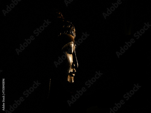 The face of Buddha in profile made of wood slightly illuminated