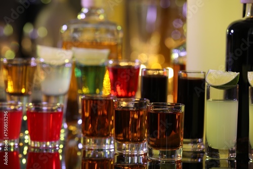 Different shooters in shot glasses and bottles on mirror surface against blurred background. Alcohol drink