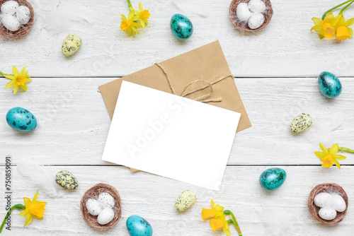 Easter greeting card in frame made of spring yellow Narcissus flowers and easter colorful eggs on white wooden background. Flat lay. Mock up. Top view with copy space