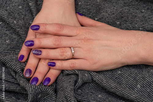 Well-groomed woman's hands resting on a uniform gray towel. Purple glitter nail polish with freshly applied. Brilliant trilogy diamond ring. Beautiful manicured hands. Selective focus and Copy space.