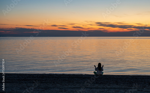 A teenage girl is meditating and exercising on the seashore watching a beautiful sunset. Sithonia, Greece, Halkidiki. Paradisos Beach in Neos Marmaras. 