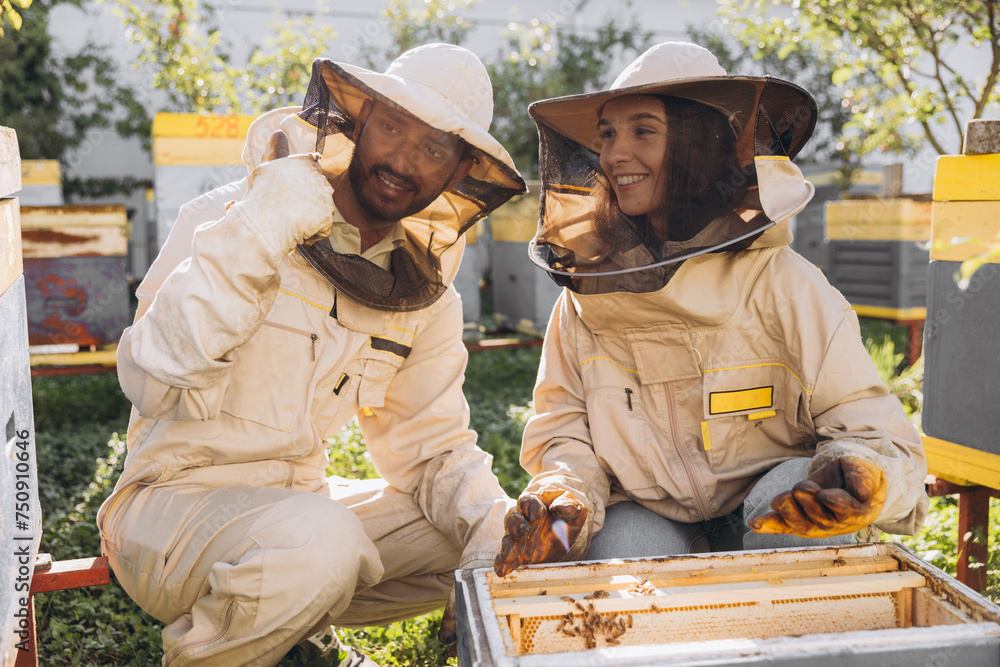 Couple of happy smiling beekeepers working with beekeeping tools near beehive at bee farm Couple of happy smiling beekeepers working with beekeeping tools near beehive at bee farm