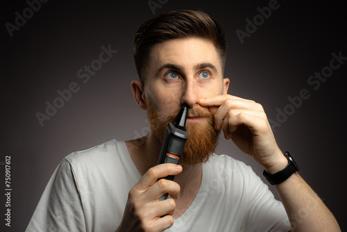 Self-care for men. Handsome young man remove hair from his nose with trimmer