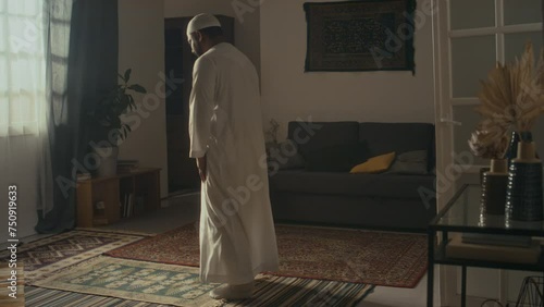 Rear wide footage of unidentified religious man in white cap and thawb making ruku and taking sujud position while expressing gratitude to Allah on prayer mat at home photo