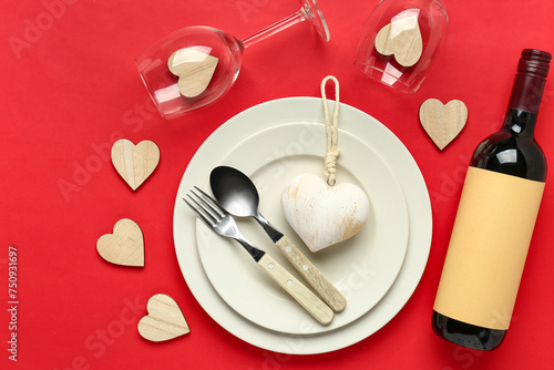 Beautiful table setting for Valentine's Day with wine bottle and decor on red background