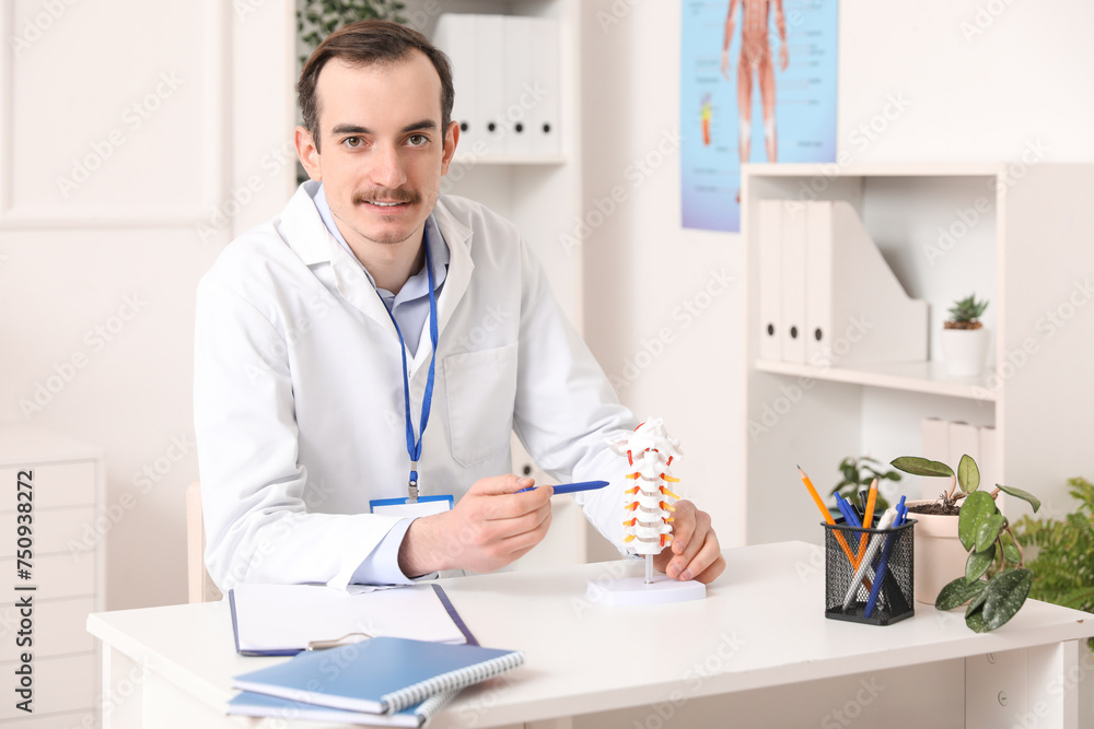 Male doctor demonstrating spinal anatomy with vertebral column model in clinic Male doctor demonstrating spinal anatomy with vertebral column model in clinic