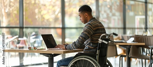 young man in wheelchair with computer working at desk photo