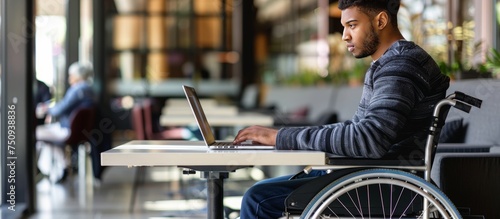 young man in wheelchair with computer working at desk