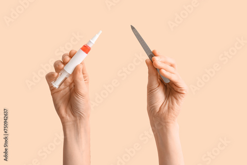 Female hands with cuticle oil pen and nail file on beige background