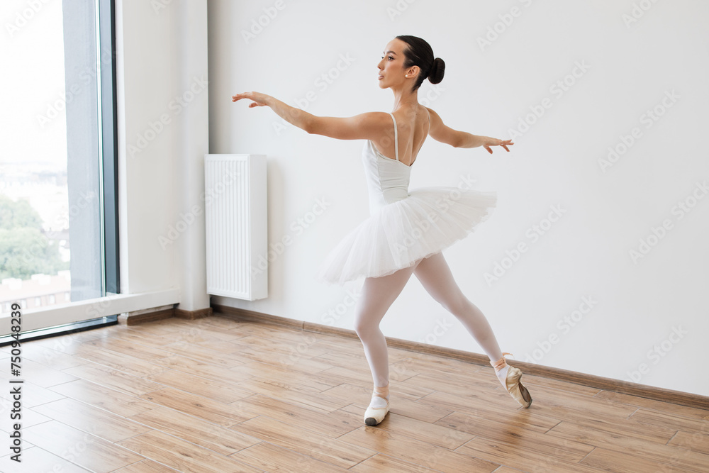 Ballet class training, high-key soft toning. Classical Ballet dancer side view. Beautiful graceful ballerina practice ballet positions in white tutu skirt near large window in white light hall. Ballet class training, high-key soft toning. Classical Ballet dancer side view. Beautiful graceful ballerina practice ballet positions in white tutu skirt near large window in white light hall.
