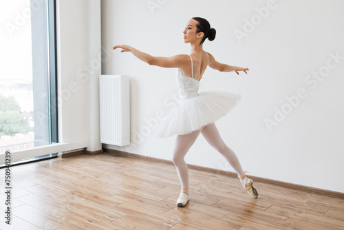 Ballet class training, high-key soft toning. Classical Ballet dancer side view. Beautiful graceful ballerina practice ballet positions in white tutu skirt near large window in white light hall.