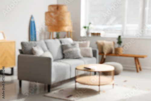Stylish interior of light living room with comfortable sofa, table, carpet and lamp, blurred view