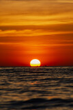 the big sun sets behind the horizon, a beautiful sea sunset. view low over the water. Bright red, orange sky over the ocean