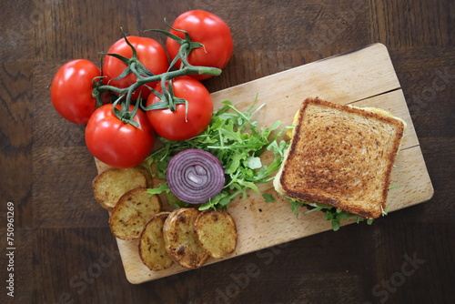 topview flatlay of delicious toasted club saandwich with vegetables dressing and baked potatoes on a wooden board