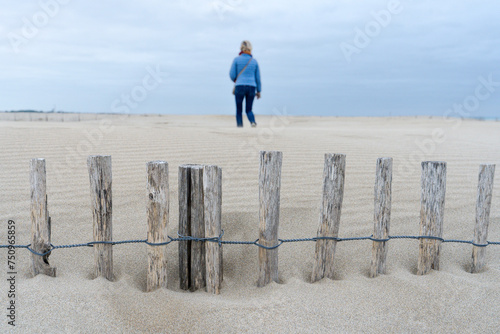 une barrière en bois ensevelie dans le sable avec une personne de dos en fond
