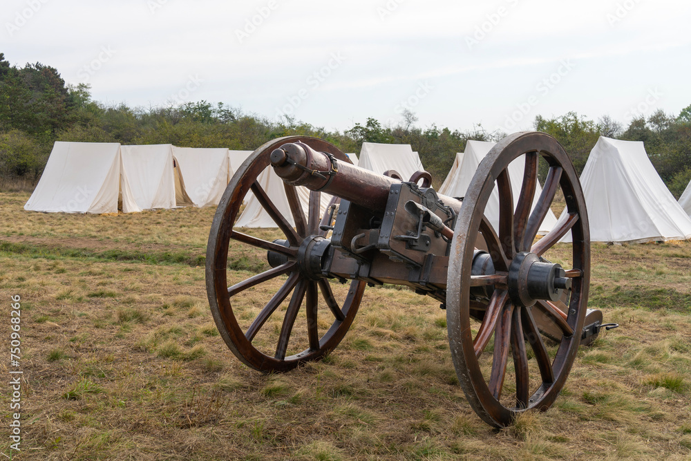 Six-pounder 19th century Hungarian cannon in front of a military camp made of white tents