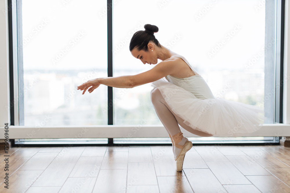 Classical Caucasian Ballet dancer side view. Beautiful graceful ballerina in white practice ballet plie positions near large window in light hall. Ballet class training, copy space. Classical Caucasian Ballet dancer side view. Beautiful graceful ballerina in white practice ballet plie positions near large window in light hall. Ballet class training, copy space.