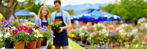 Couple working in garden center with colorful flowers in pots for sale in spr...