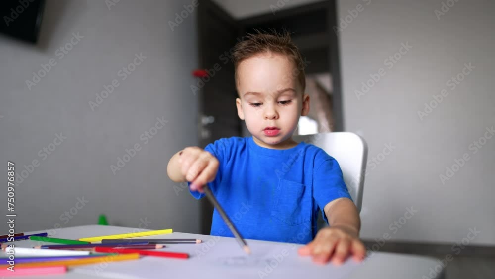 Charming baby boy sitting at desk holding a pencil. Cute kid drawing and talking. Blurred backdrop. Charming baby boy sitting at desk holding a pencil. Cute kid drawing and talking. Blurred backdrop.