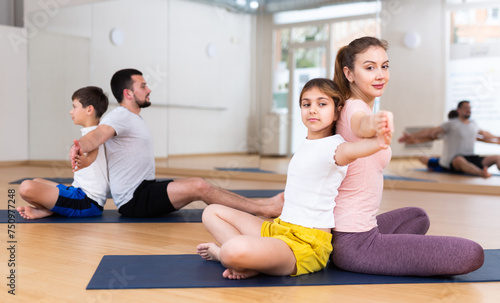 Children and parents sitting back to back on yoga mats and doing exercises together.