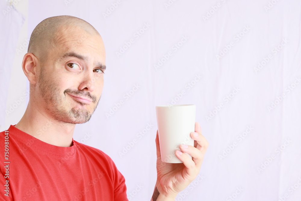 expressive bald man in red tshirt , drinking in a white cup expressive bald man in red tshirt , drinking in a white cup