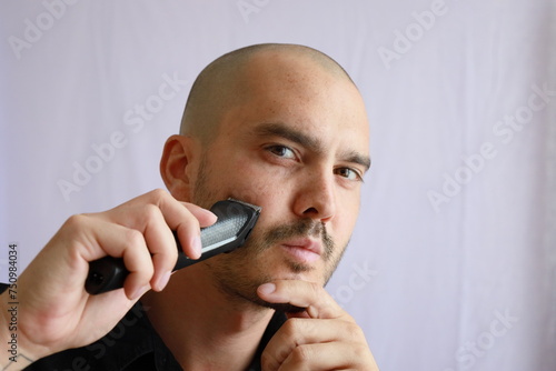 bald man using an electric shaver to trimm his hair and beard