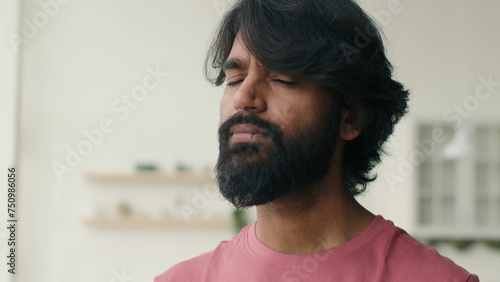 Close up front view adult 30s multiracial Arabian Indian ethnic bearded man serious millennial closing eyes. Male head shot portrait of calm middle-aged muslim guy homeowner home renter alone indoors