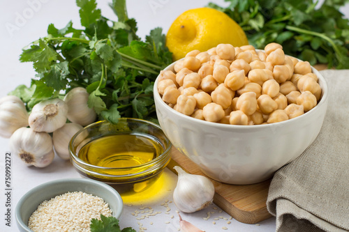 Chickpeas in a bowl, lemon, olive oil, sesame, cilantro, garlic on a wooden board, on a light background. The process of making hummus. Eastern cuisine. Horizontal.