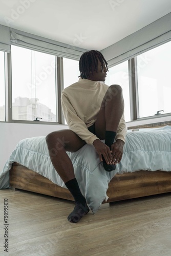 Man with dreadlocks wearing vintage clothing sitting on the bed © sashapritchard
