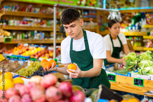 Hardworking young salesman working in a vegetable store puts fresh oranges on the counter for sale