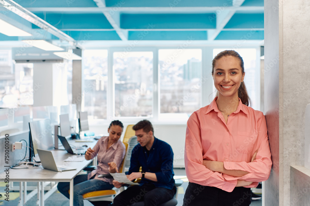 Obraz premium Portrait of young smiling business woman in creative open space coworking startup office. Successful businesswoman standing in office with copyspace. Coworkers working in background