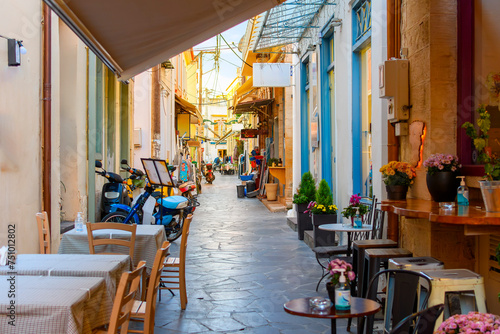 Fototapeta Naklejka Na Ścianę i Meble -  A narrow alley full of sidewalk cafes and shops in the historic old town of Aegina, Greece, on the island of Aegina, one of the Greek islands in the Saronic Gulf.